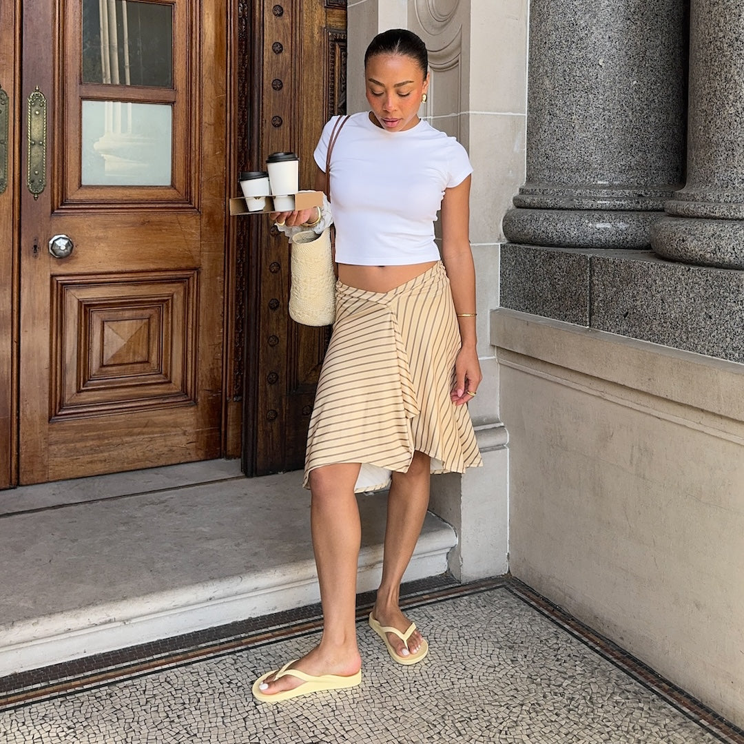 woman in white tshirt and beige skirt wearing lemon flip flops 
