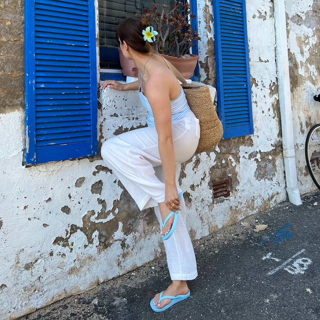 woman in stripey singlet and white pants wearing sky blue flip flops 